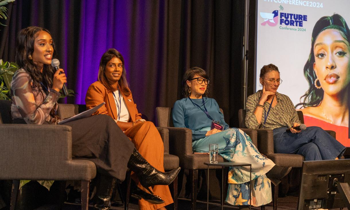 Panel discussion on stage. Four women on chairs holding microphones
